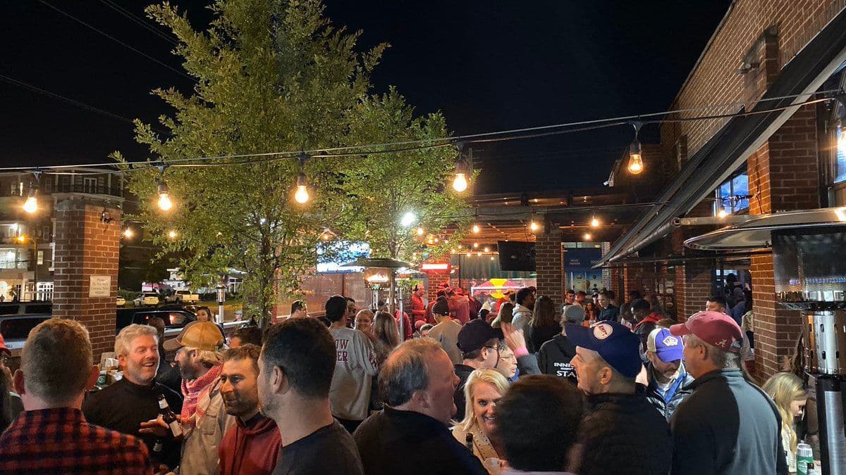 A packed gameday crowd under string lights on the Innisfree patio